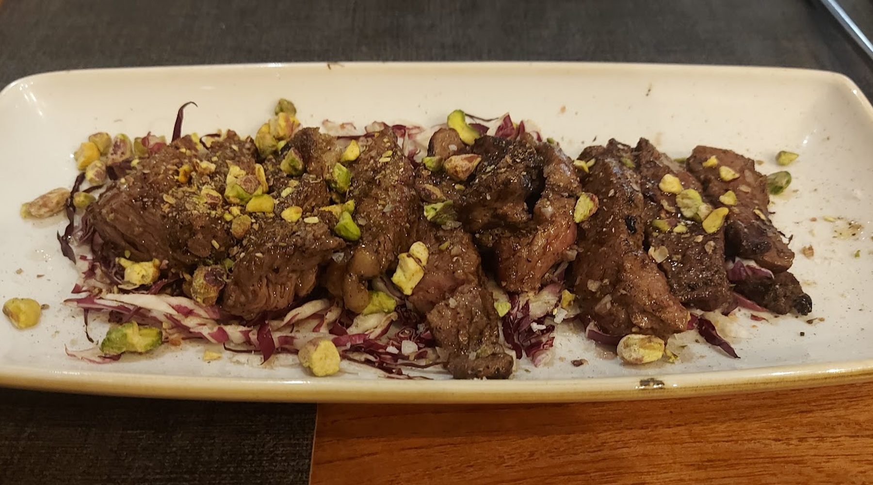Tagliata di manzo affettata su radicchio, con granella di pistacchio, servita su un piatto lungo
