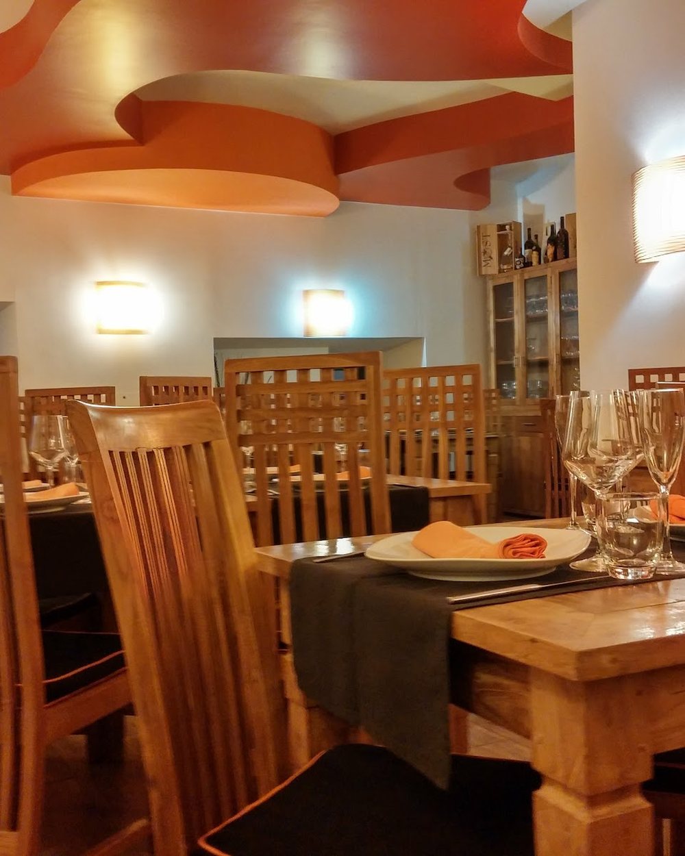 La sala interna di 80 Fame: tavoli in legno chiaro apparecchiati con tovaglioli arancioni, sedie a schienale alto e il soffitto dipinto ad onde arancioni