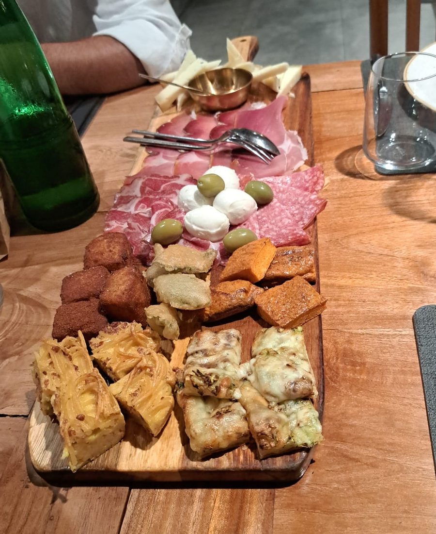 Tagliere lungo di legno con salumi, mozzarelline, olive, frittelle e formaggio fuso